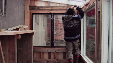 greenhouse construction - man assembling wooden interior by the window