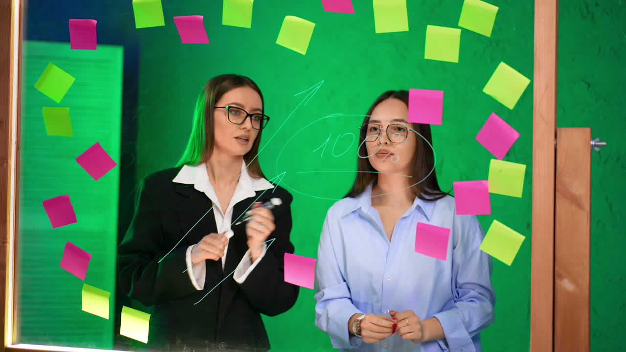 Pros brainstorming with sticky notes. Two women brainstorm ideas on a glass surface covered in colorful sticky notes in a modern workspace