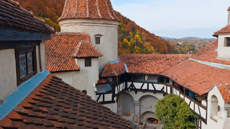 decks and roofs of the beautiful medieval castle bran in brasov, romania. red tiles covering the old rooftops. colorful autumn nature at backdrop.