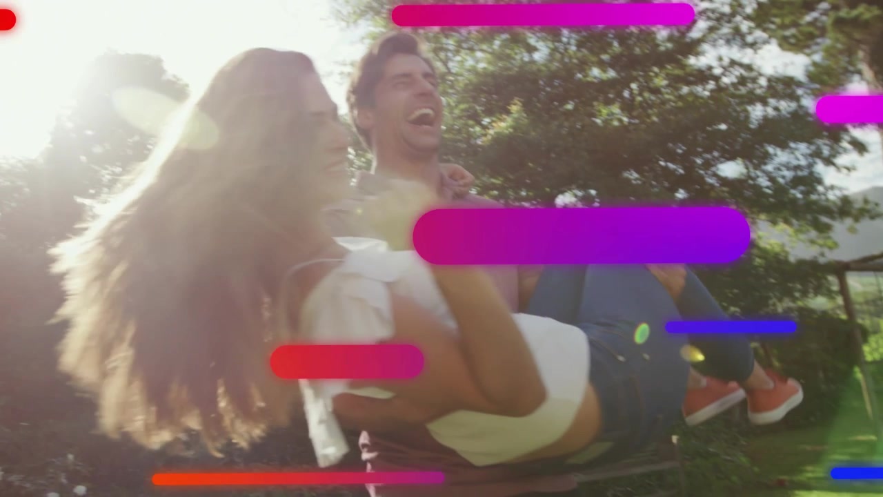 Homem levantando mulher em um parque ensolarado, girando e segurando, enquanto barras de cores sobrepõem o quadro para anúncios de romance.