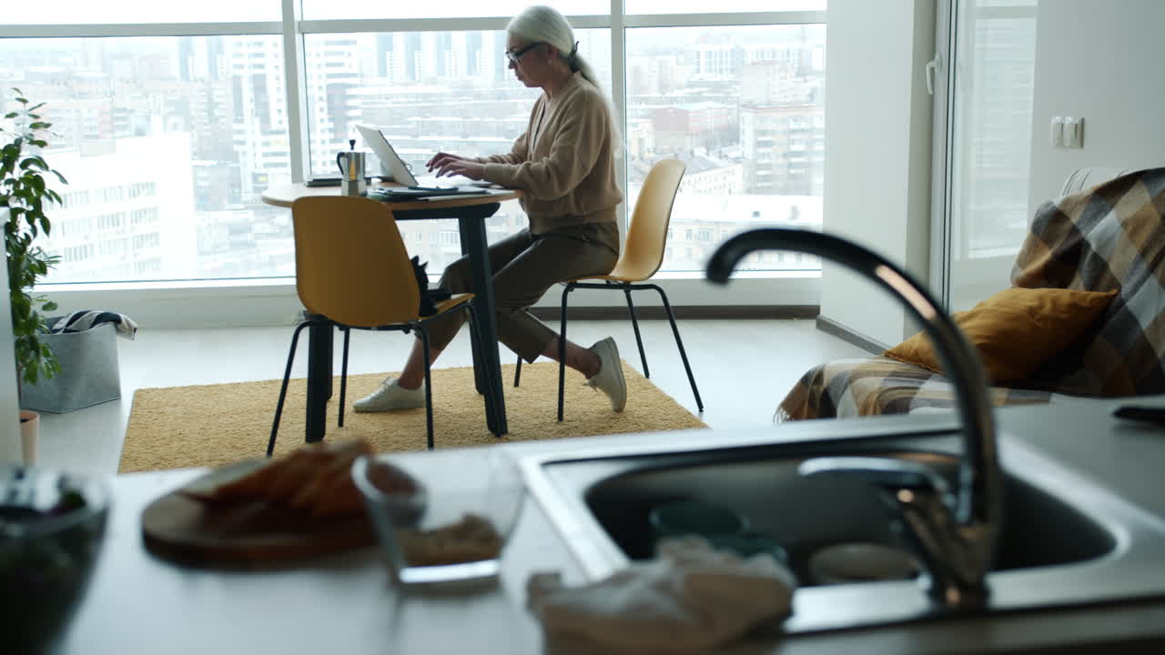 Kvinde arbejder hjemmefra ved et spisebord med byudsigt