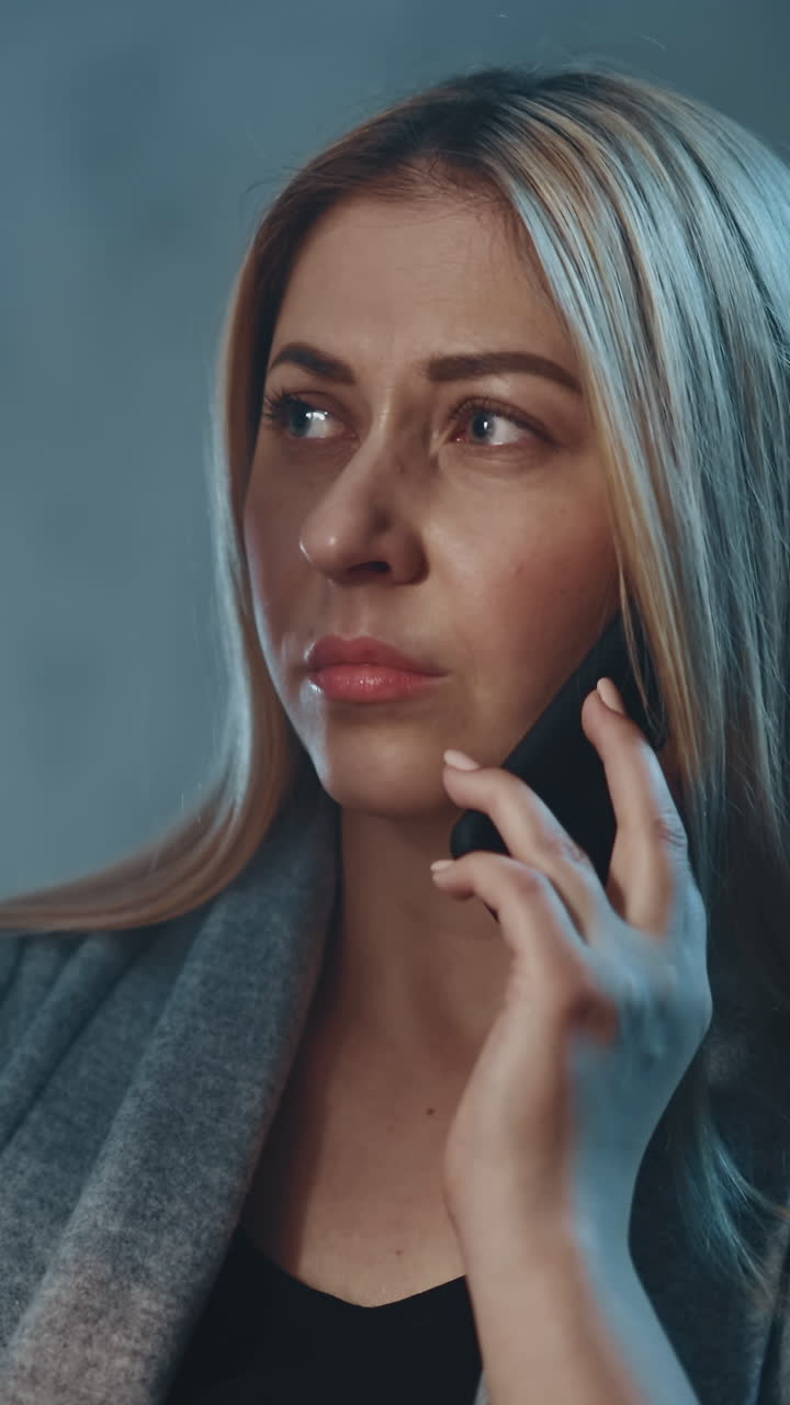 Pensive blonde female patient talks on mobile phone with doctor looking at x-ray picture in shady apartment room in evening close view slow motion