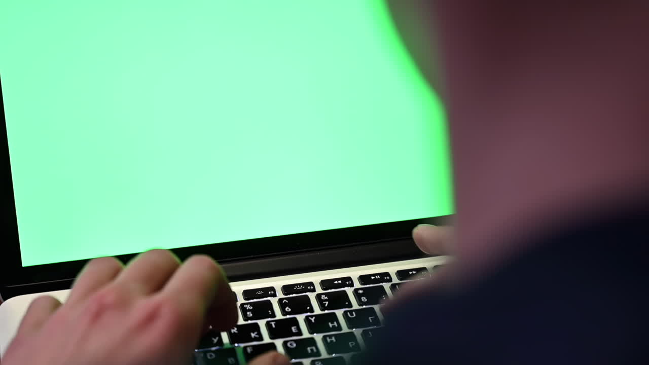 Close up of a man typing on a laptop with a green screen