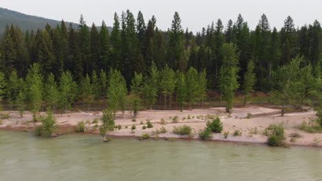 Aerial-shot-of-a-forested-bank-alongside-the-Flathead-river,-Montana,-smoke-fills-the-sky-in-the-background-from-nearby-wildfire,-camera-dolly-moves-to-the-right