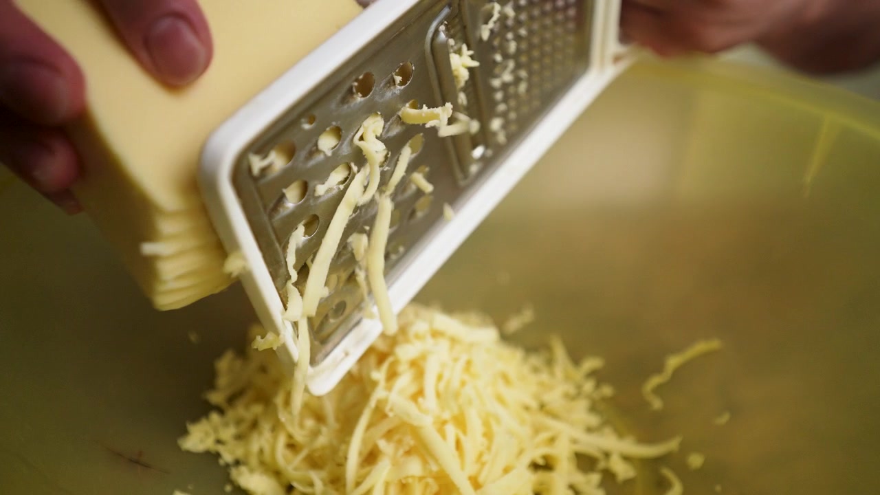 Un primo piano dettagliato di uno chef che grattugia abilmente il formaggio. Il processo manuale evidenzia la precisione culinaria e la preparazione di ingredienti freschi.