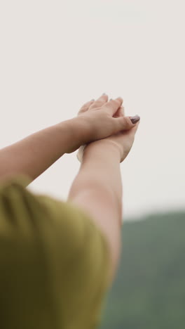 woman catches rain drops and spreads onto hands against distant green sloppy hill at eco resort on nasty day backside view slow motion