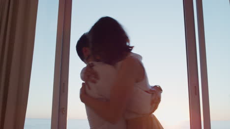 happy-travel-couple-arriving-in-hotel-room-on-honeymoon-vacation-looking-out-window-enjoying-beautiful-view-of-ocean-at-sunset-embracing-sharing-romantic-holiday
