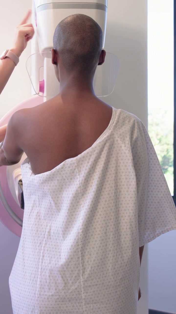 Video verticale: Mani che entrano e regolano dischi rosa protettivi in una clinica, con un paziente che indossa un camice monospalla per la scansione.