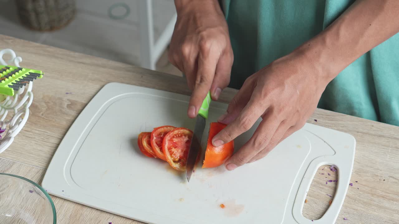 Bir adam, salata için sulu ve olgun bir domatesi kesme tahtasında dilimliyor.