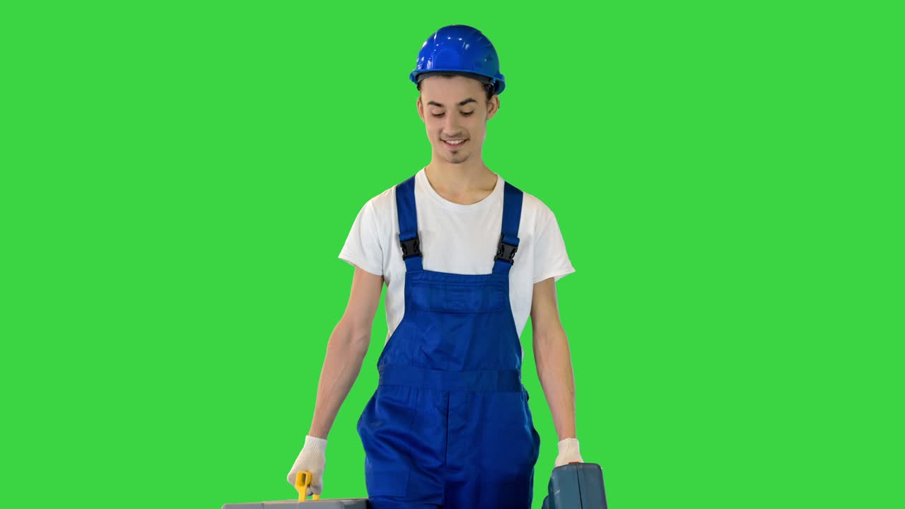 Young construction worker is walking to you with his two toolboxes on a Green Screen, Chroma Key