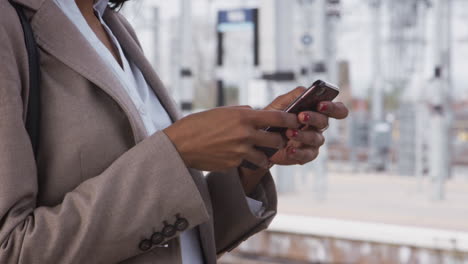 close up of businesswoman commuting to work standing on train platform using mobile phone