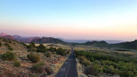 Vista-Aérea-Delantera-Del-Desierto-De-Utah-Y-El-Pavimento-De-La-Carretera-Con-Paisaje-Montañoso-Cerca-Del-Condado-Central-De-Escalante-Garfield,-Estados-Unidos