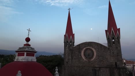 iglesia del calvario in cuernavaca showcasing stone facade, twin red spires, and dome with cross under a dim evening sky with the moon visible, morelos, mexico