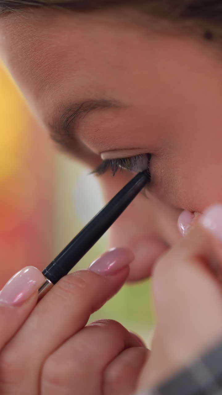 Teen applies eyeliner, Young woman concentrates while defining her lower waterline with pencil, Teen girl skillfully uses small strokes to line her lower waterline during makeup application