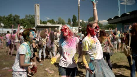 three young multi-ethnic girlfriends are throwing colourful powder on holi festival in daytime in summer, laughing, friendship concept, color concept