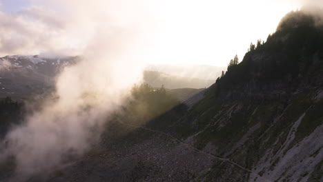 Golden-ray-of-light-cuts-across-mountain-ridgeline-illuminating-cloud-with-beautiful-sunflare,-aerial-dolly