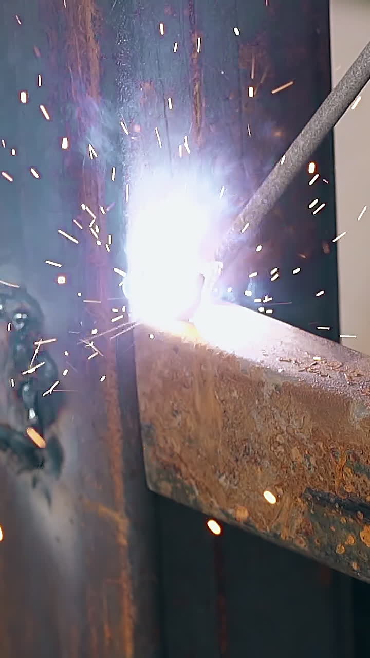 closeup skilled worker uses modern welding instrument for connecting metal fence carcass at sparks