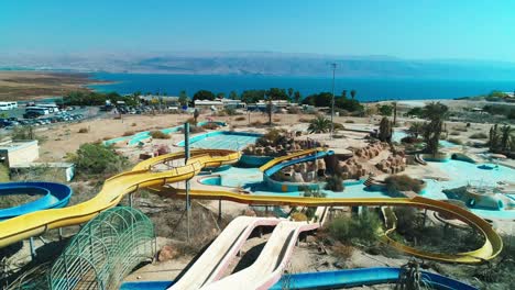 drone shot of a couple sitting on a water slide in an abandoned park, in front of the dead sea