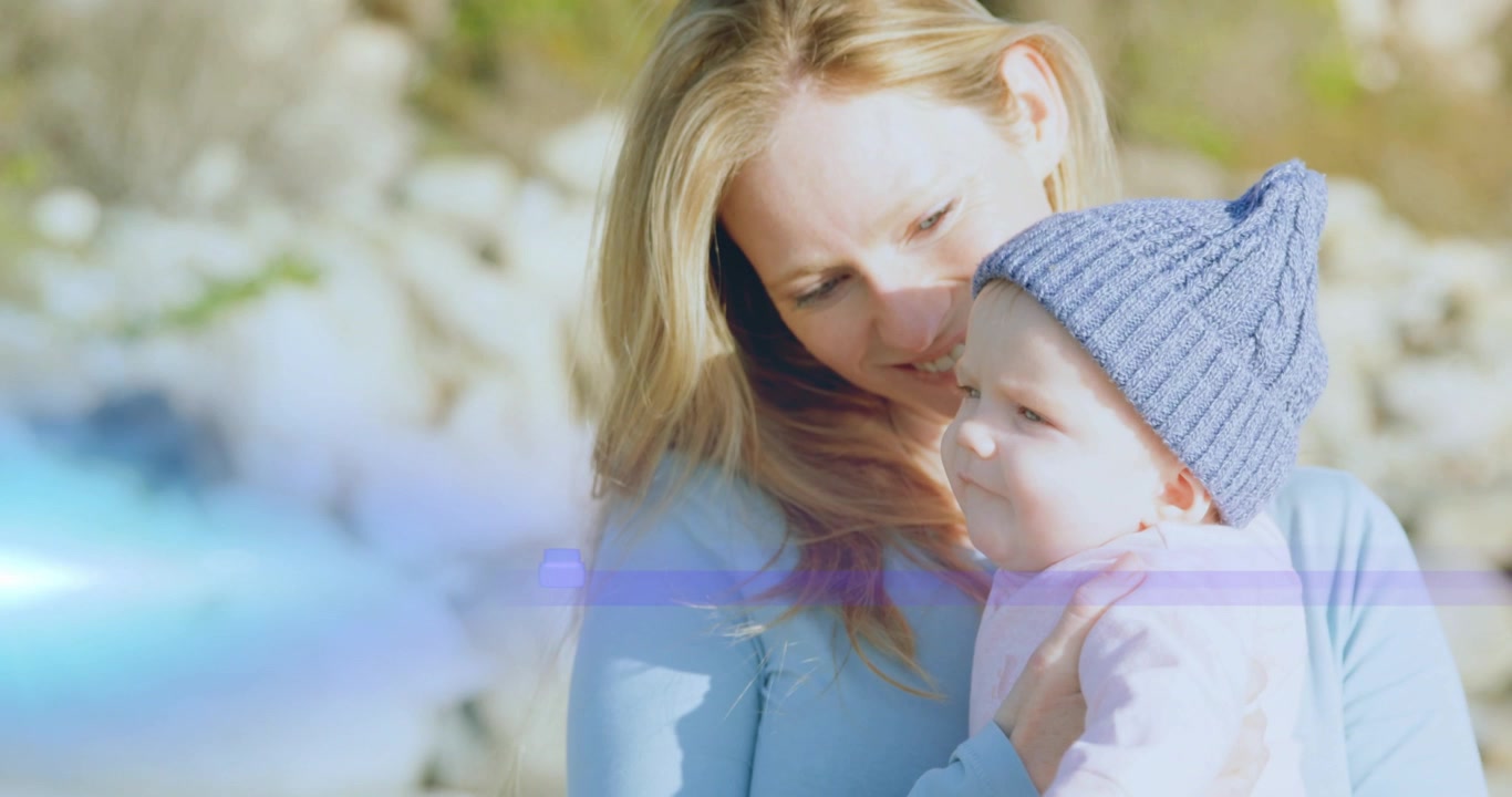 Mutter hält Säugling liebevoll für dessen Wohlbefinden, während das Baby sich einem externen Reiz zuwendet, mit Lens Flare.