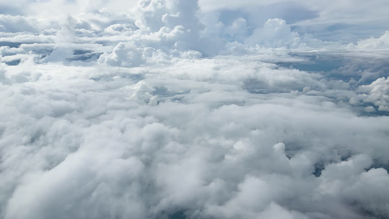 Smooth aerial flight over bright cumulus cloudscape, distant horizon visible through airplane window, minimal movement