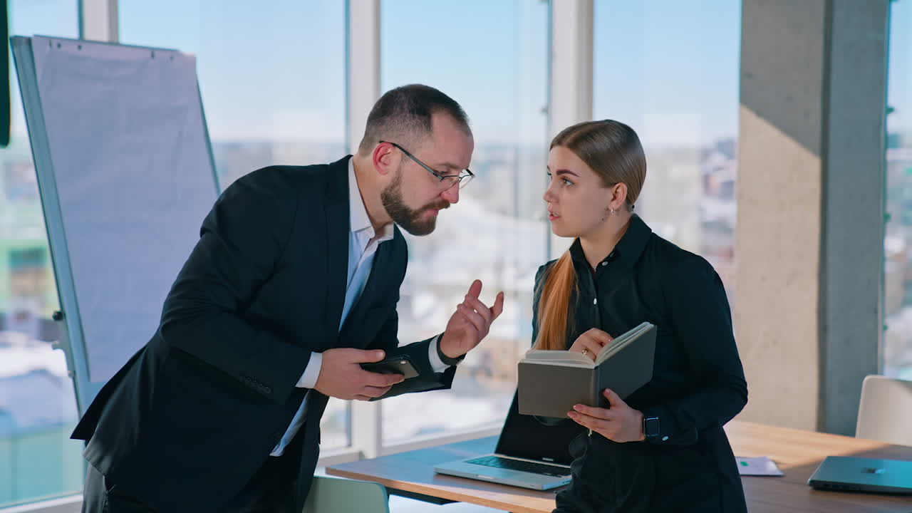 Business colleagues in the light office. Entrepreneur in black suit talking with his female secretary. Large window with city background.