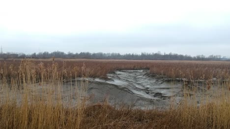 Aerial-push-in-dried-up-wheat-river-bed-muddy-landscape-cloudy-dark-swamp-day