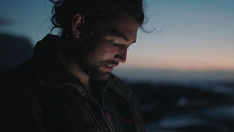 hombre joven enviando mensajes de texto en el teléfono inteligente cerca de la playa temprano en la noche