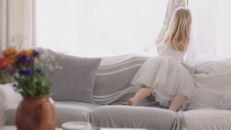 beautiful little girl sitting on sofa looking out window having fun child in playful mood enjoying weekend morning at home