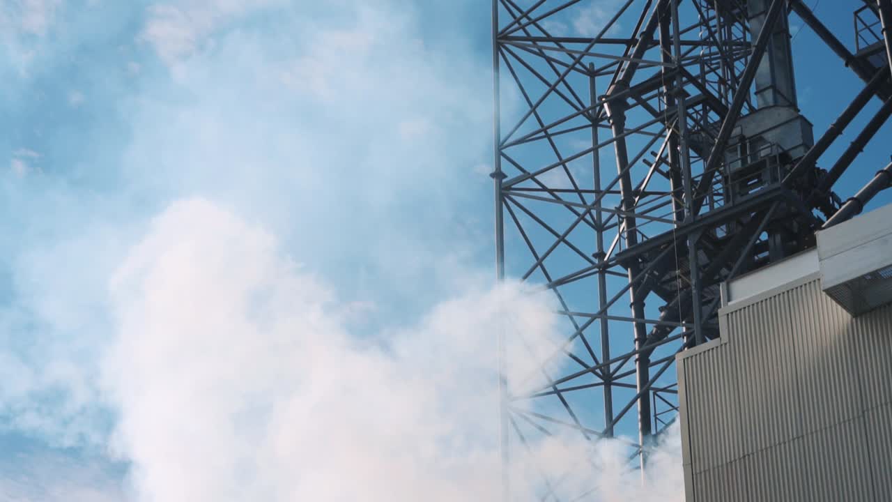 Intense plume of white smoke in a factory. Derrick with a pipe and metal structures of the plant. Environmental pollution. Ecology