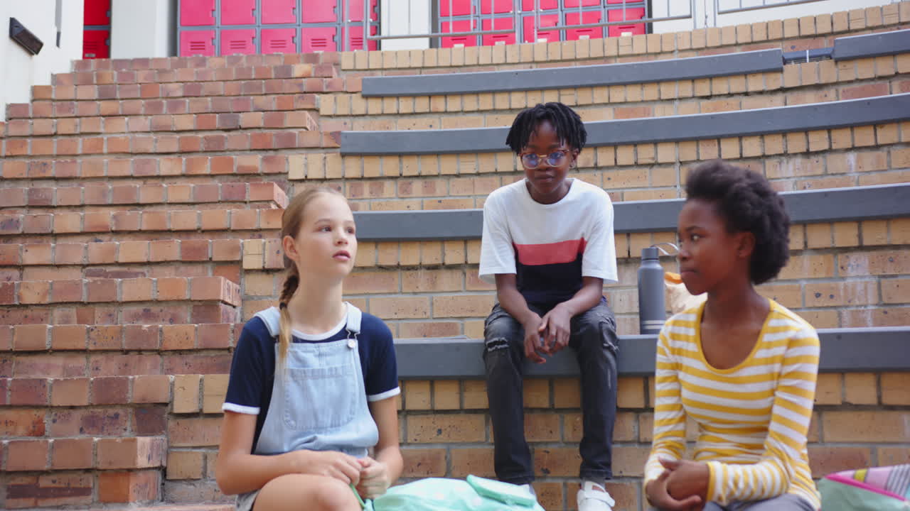 Sitting on steps, three school girls talking and enjoying break time together