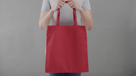 mujer caucásica con camiseta blanca sosteniendo una bolsa roja sobre un fondo gris, espacio de copia, cámara lenta