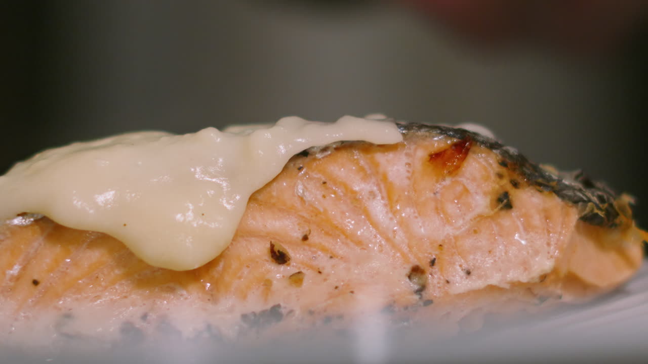 Filé de salmão escocês assado com molho cremoso, sendo cuidadosamente colocado pelo chef. Close-up da textura desfiada, vapor e empratamento gourmet. Conteúdo sobre dieta mediterrânea e culinária nutritiva, clipe em 4K.