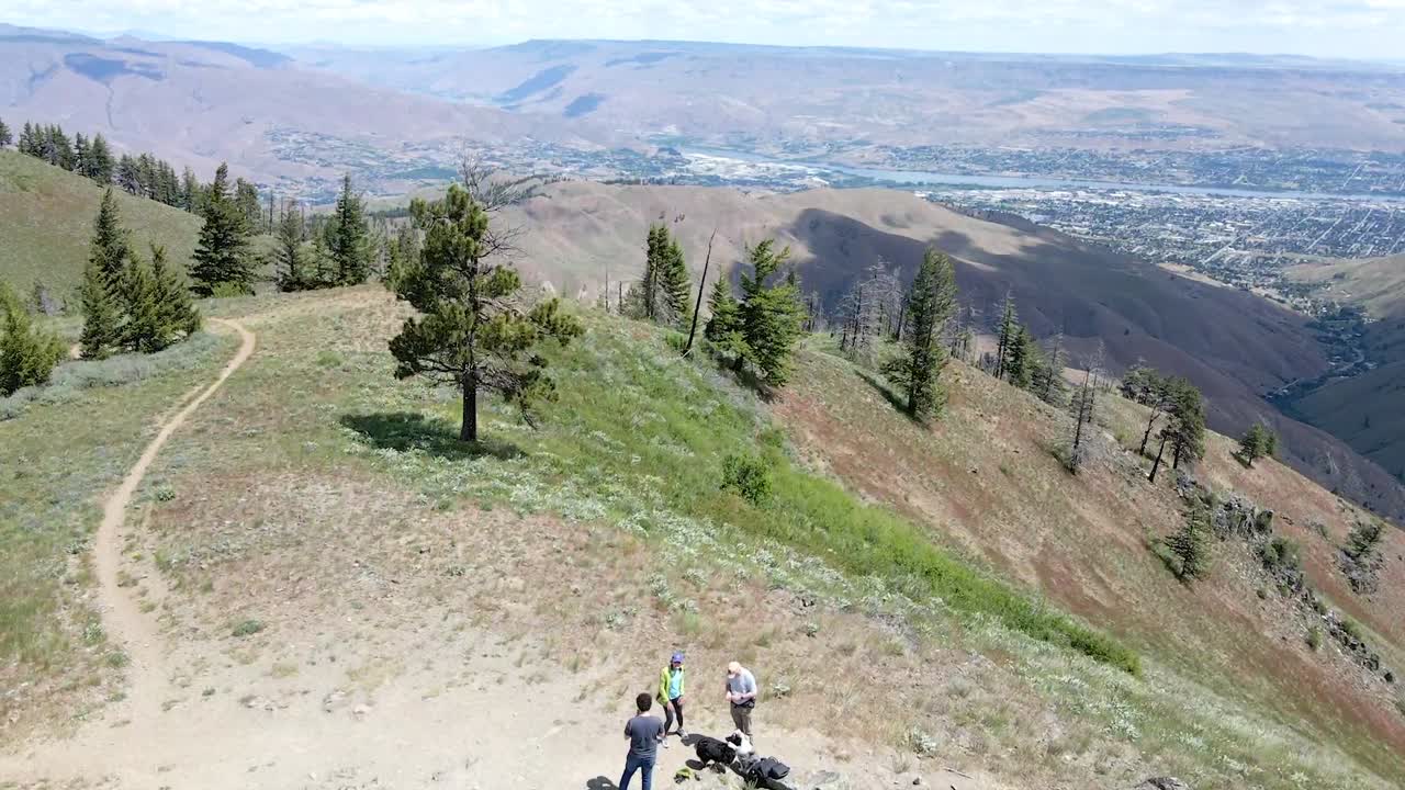 Aerial ascending reveal shot of people hiking in top of a mountain of Wenatachee with the Columbia river in the horizon.
