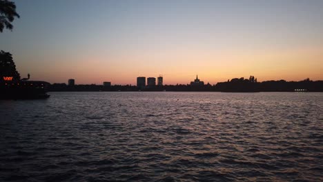 Waves-on-Herastrau-Lake,-Bucharest-at-sunset-with-distant-buildings-on-background