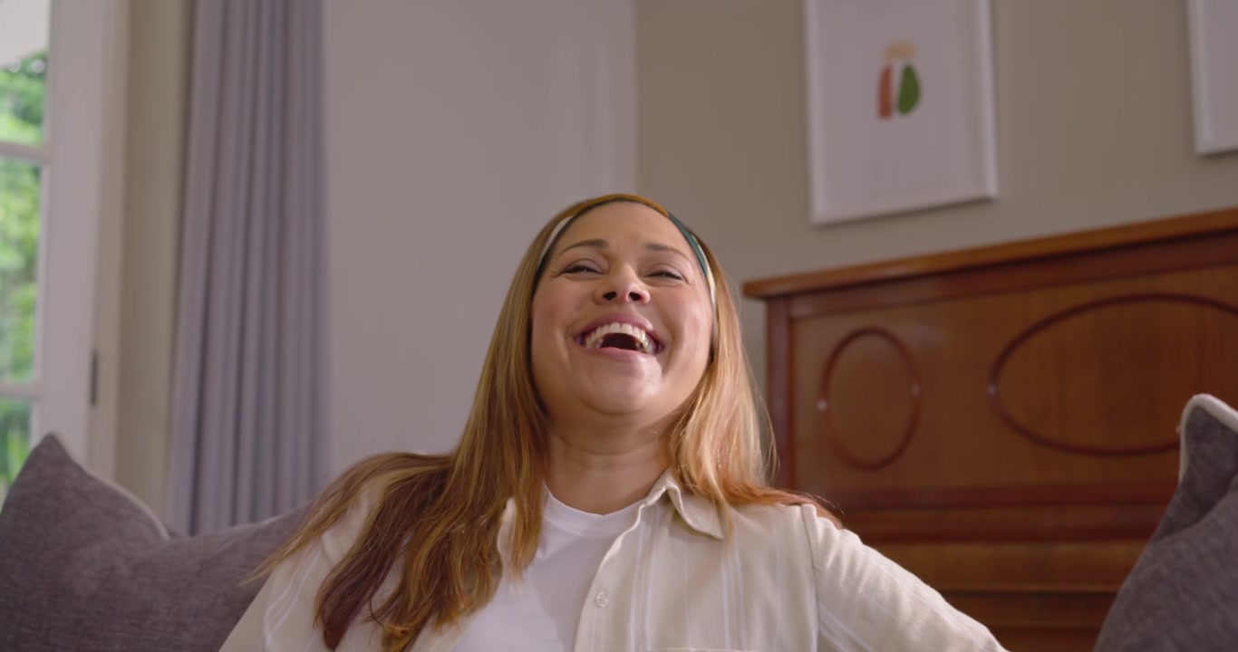 Donna afroamericana che sorride, girandosi verso la telecamera sul divano, reagendo all'inquadratura che si stringe e ridendo.