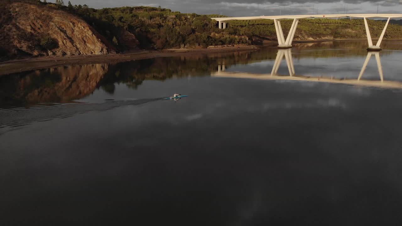 Aerial side view of man paddling blue canoe on river towards bridge