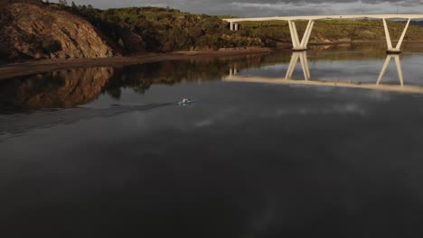 aerial side view of man paddling blue canoe on river towards bridge