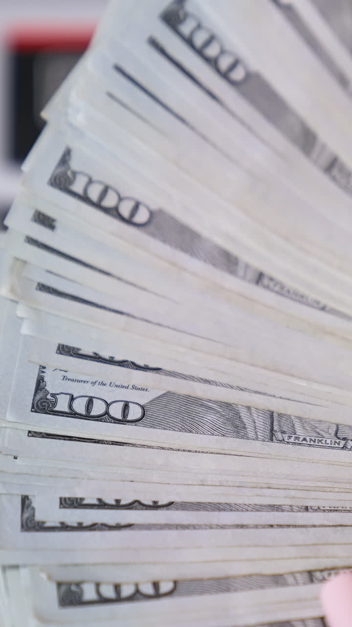 Usa money in woman's hands. Wad of one hundred dollar banknotes in hands on blur background of automatic counter machine. Finance concept. Close-up. Vertical video