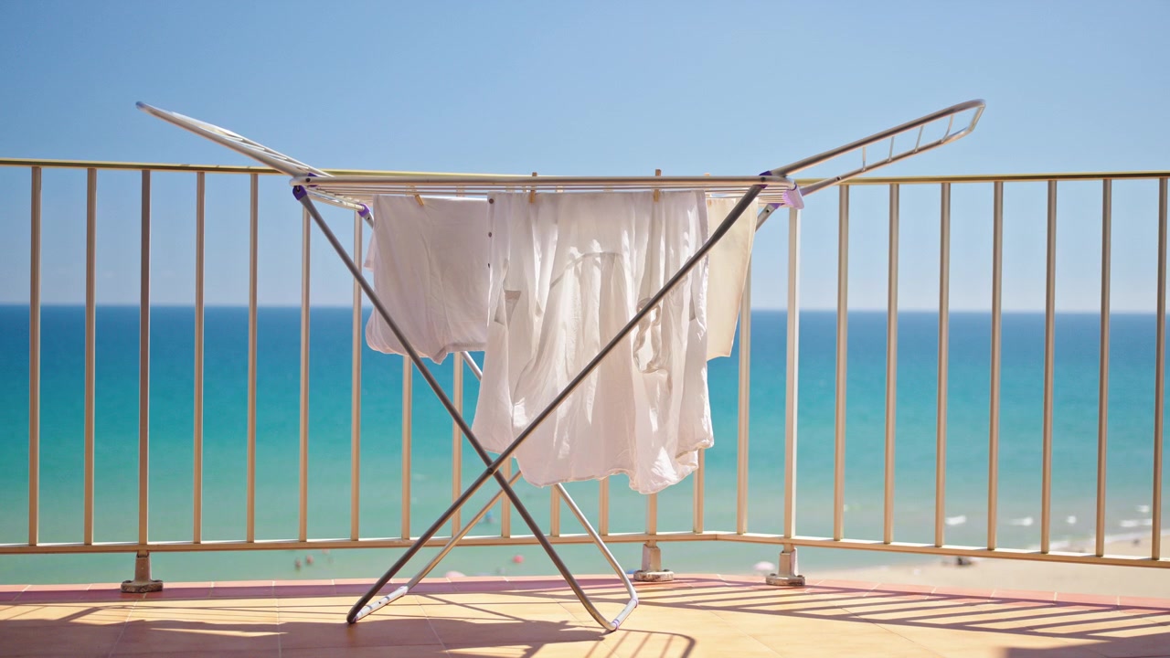 White summer clothes drying on balcony with turquoise sea view at sunny beach resort.