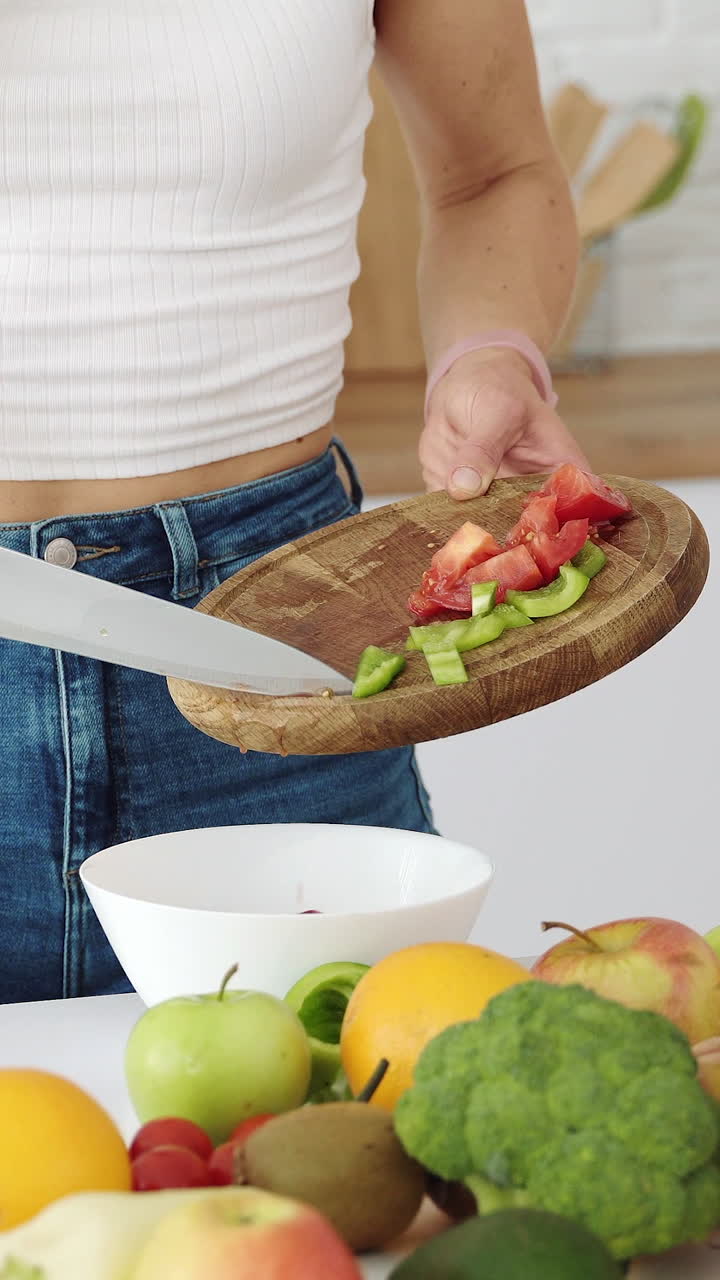 Girl mixes in a plate pepper and red tomato. Cooking a salad of fruits and vegetables. Vertical video