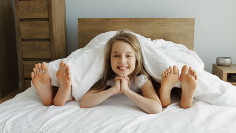 Close-up-view-of-little-girl-looking-out-of-the-blanket-and-smiling-at-camera-between-her-parents-feet