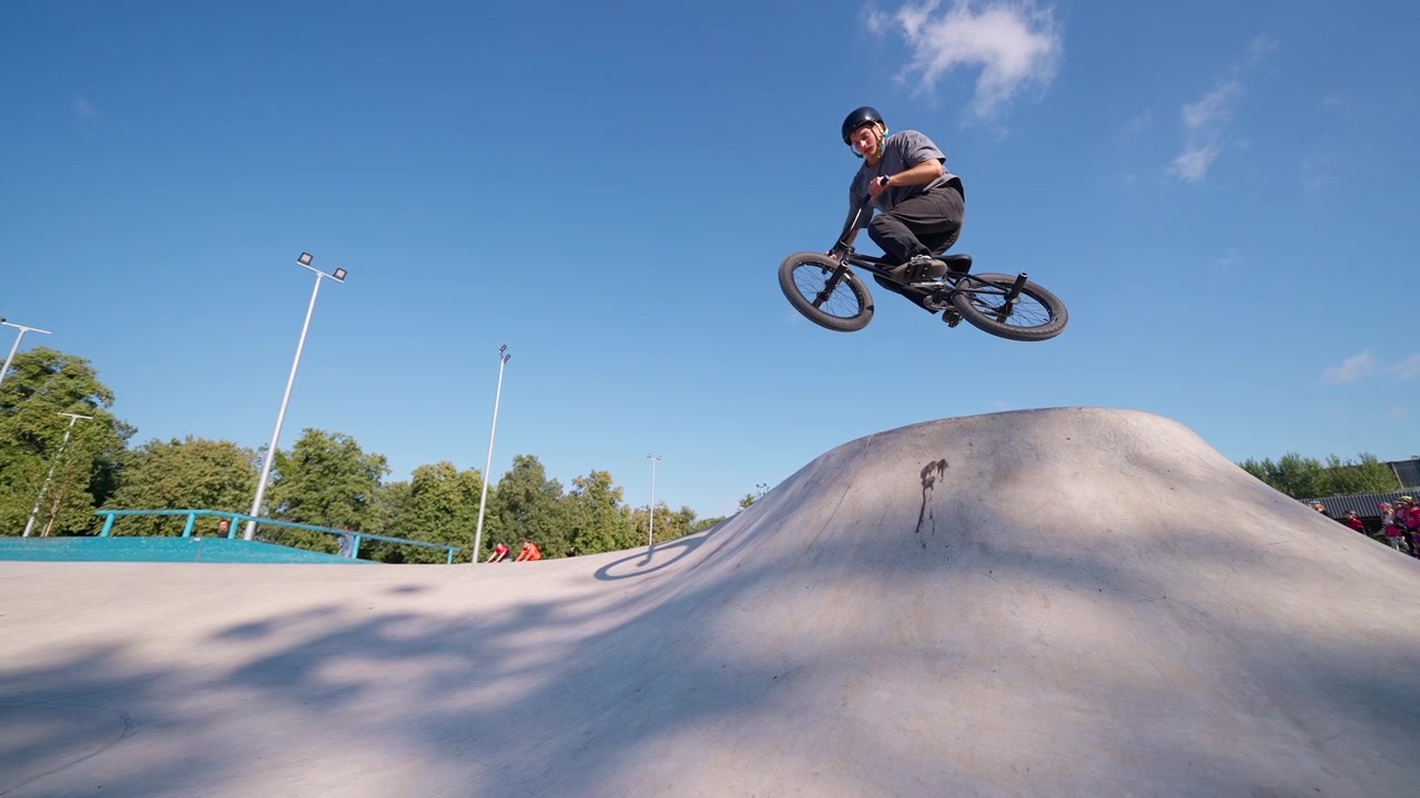 Ung mand hopper med BMX-cykel over betonpukkel i skatepark