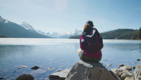 rear view of outdoor woman sitting at lakeside rock, maligne lake, pan