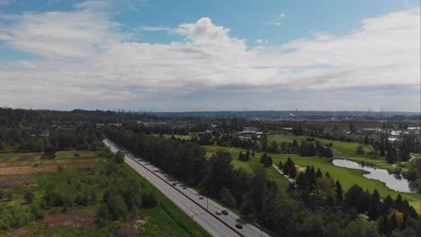 static wide drone view of golf course lush green trees grass sand dunes ponds water aerial on sunny cloudy day over highway with light traffic cars trucks moving in foreground slow pan stabilized