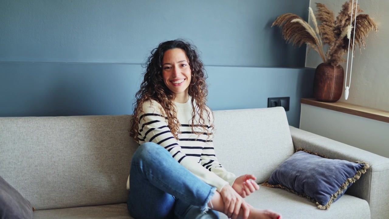 Mujer joven con cabello rizado sonriendo en un sofá