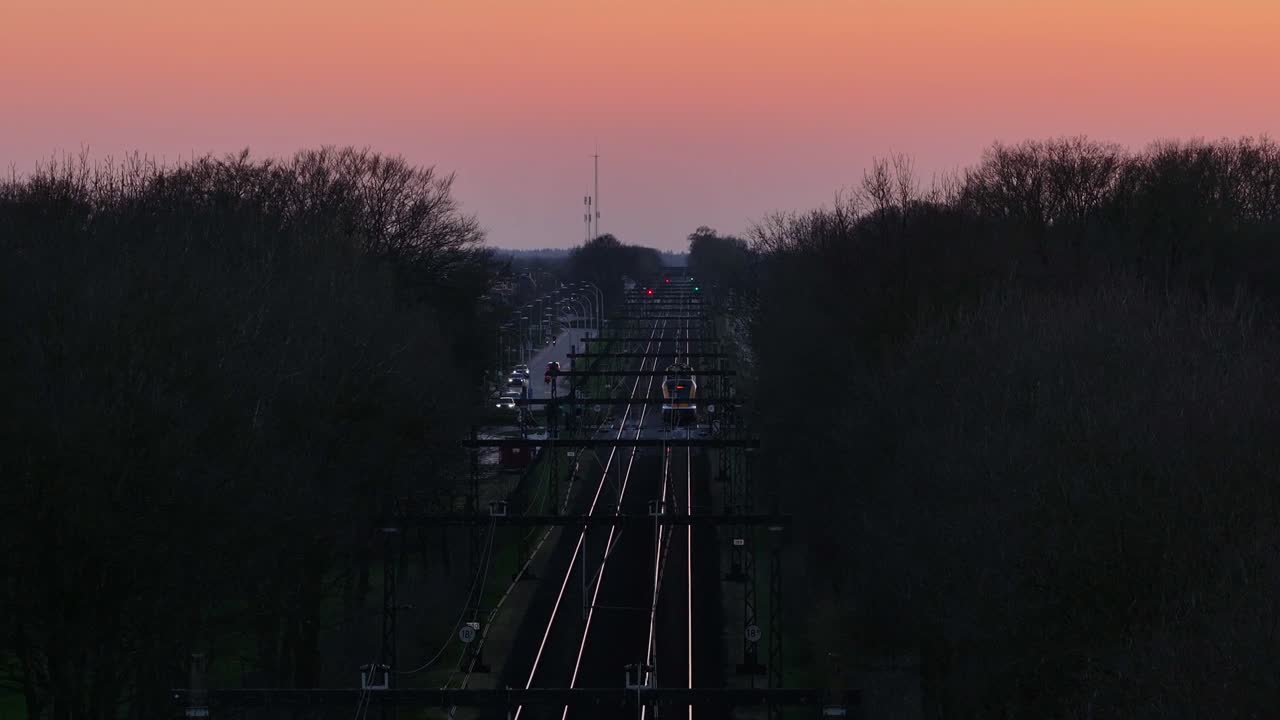 Train approaching small town at sunset with pastel sky and distant lights
