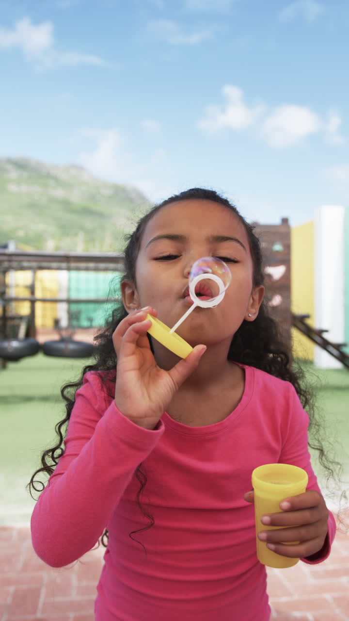 Vertical video: In this school scene, a young biracial student is blowing a bubble