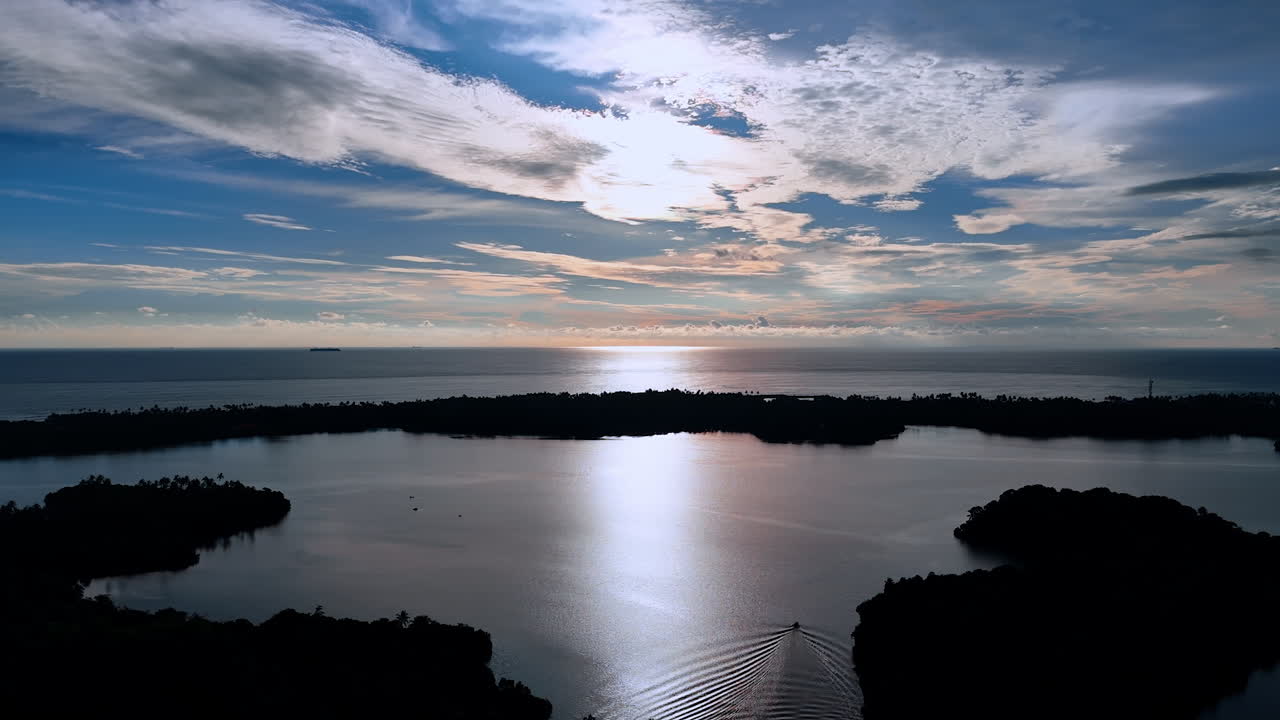 Calm waterscape surrounded by black silhouettes of plants. View of the Indian Ocean under the beautiful sky with clouds at sunset.