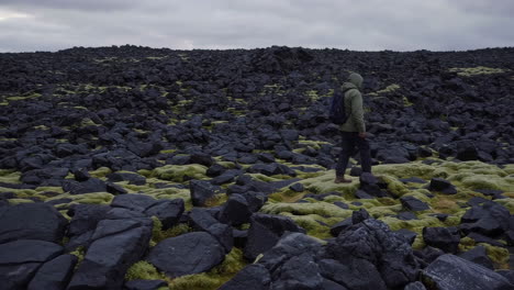 person walking through moss-covered volcanic landscape