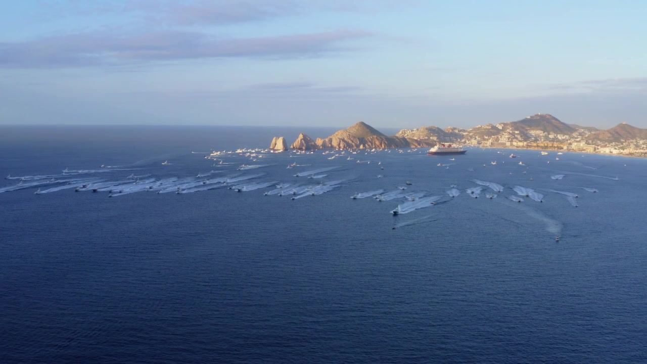 Laaja 4K-dronekuva esittelee massiivista viuhkamaista leviämiskuviota urheilukalastusveneistä kiihdyttämässä sinisen lahden poikki risteilyaluksen lähellä Cabo San Lucasissa, Los Cabosissa, Baja California Surissa, Meksikossa